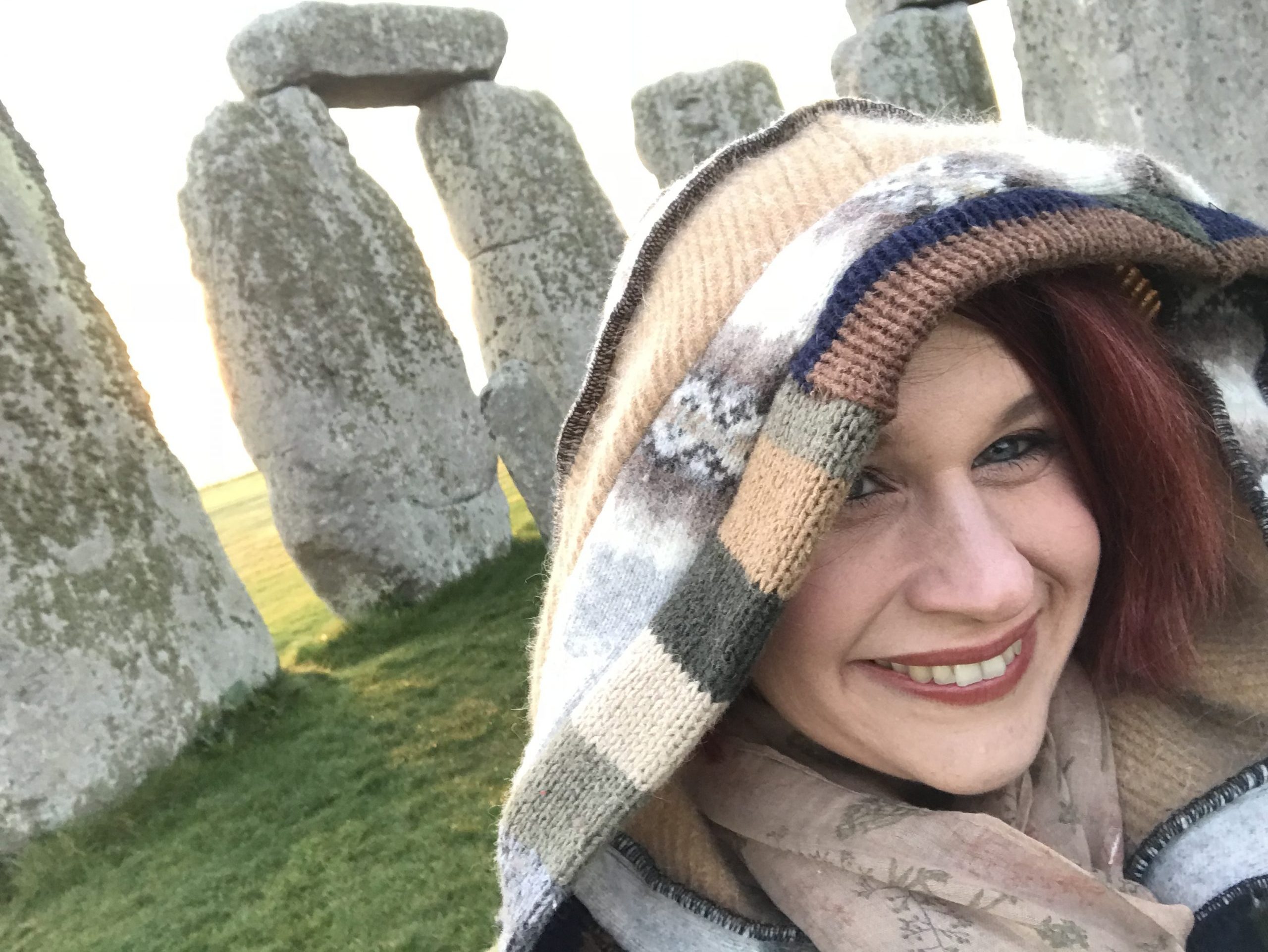 selfie of a smiling woman wearing a hood and with the Stonehenge behind her